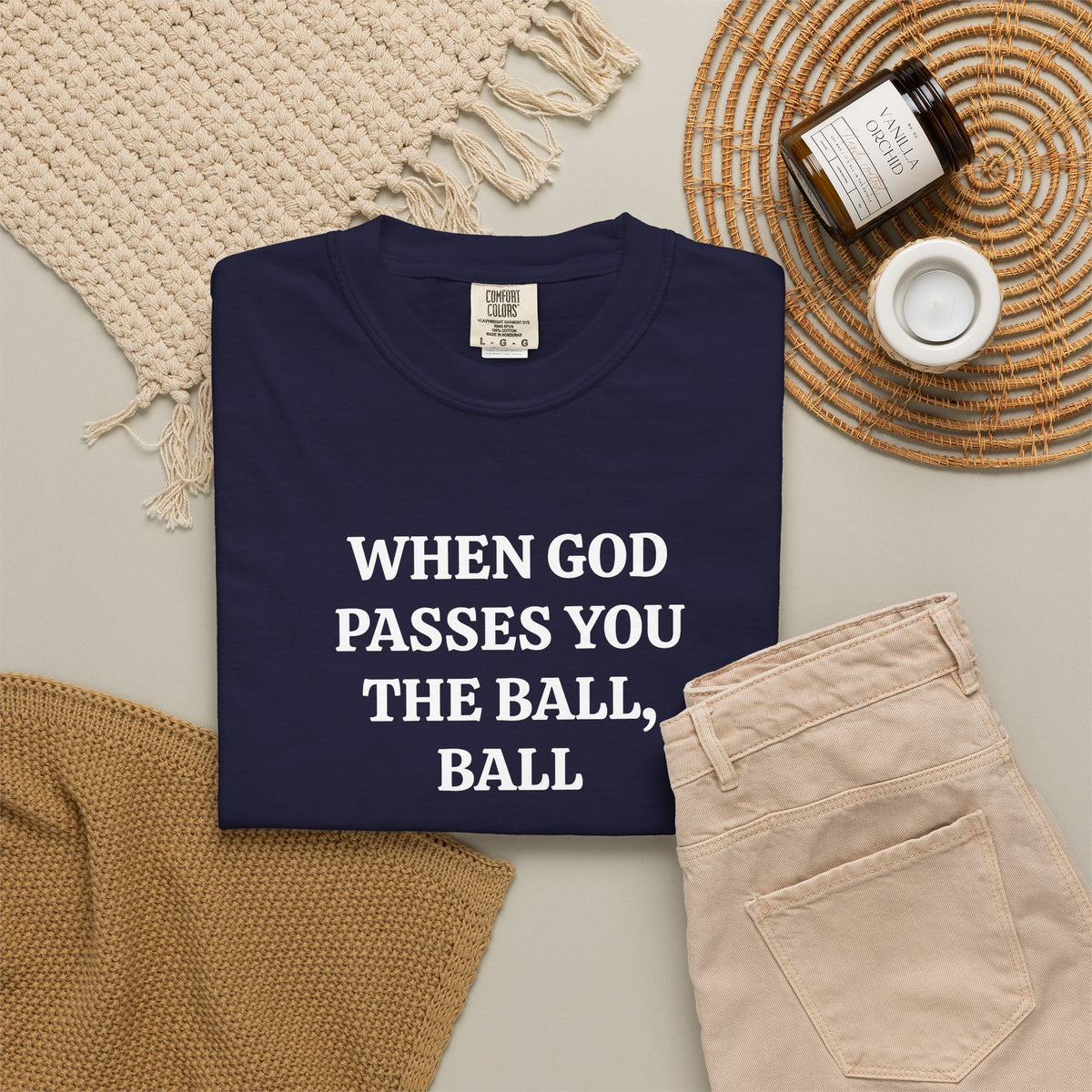 True Navy When God Passes You The Ball, Ball tee folded in a flat lay with jeans and candle