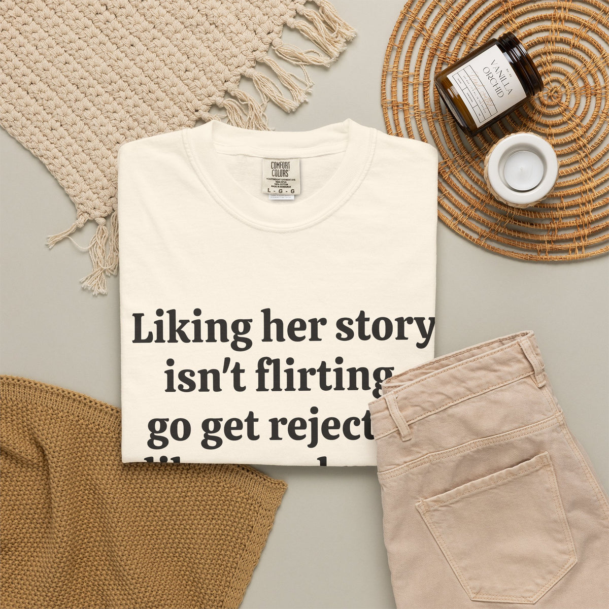 Ivory Rejected Like A Real Man tee folded in a flat lay with jeans and candle